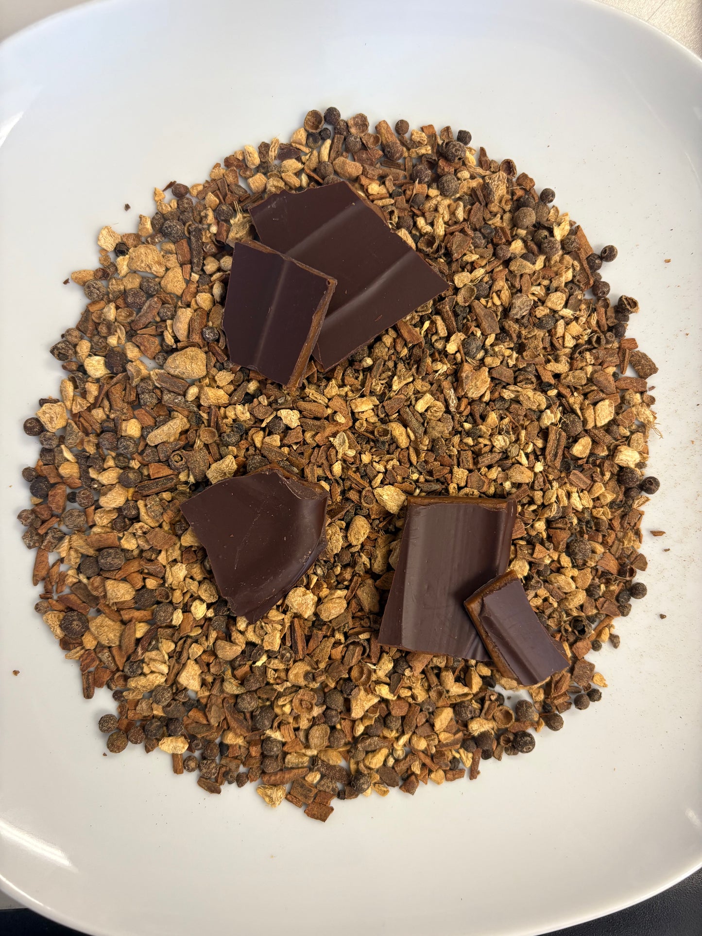 Gingerbread spices (ginger, cloves, cloves) on a white plate with 5 pieces of toffee brittle on top of the spices.
