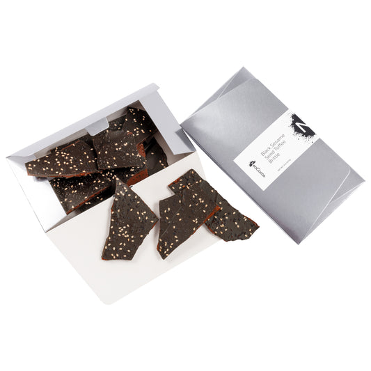 2 dimensional angle silver rectangle of opened 8oz box with title of “Black Sesame Seed Toffee Brittle” with black colored NeoCocoa logo and 8oz pile candy pieces inside the box bottom. 3 pieces of candy spilling out.