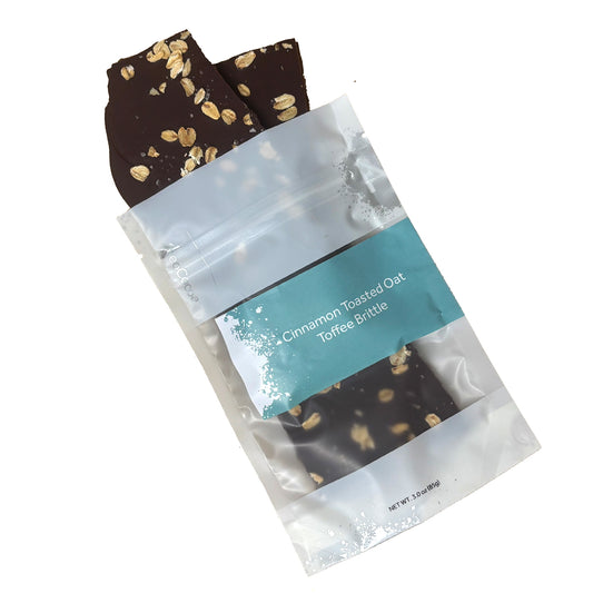 Oat brittle pieces spilling out of packaging labeled 'Cinnamon Toasted Oat Toffee Brittle' on a white background