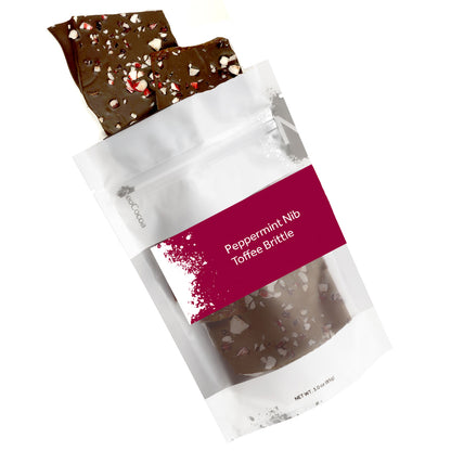 Peppermint nib brittle pouring out of 3oz sized bag with orange label stating “Peppermint Nib Toffee Brittle” and NeoCocoa logo on a white background.