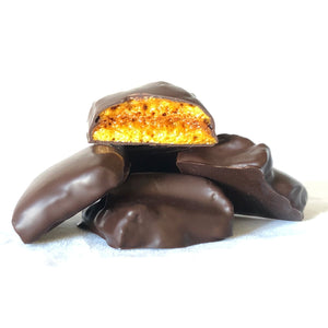 Pile of chocolate covered honeycomb candy with one piece broken open to expose honeycomb candy inside.