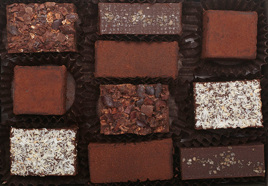 View from above and inside of the opened “Ensemble Box” with 10 chocolate truffles arranged in paper candy cups: 2 of each flavor: Almond butter, Cacao Nib, Lime, Coconut and Mocha Cinnamon