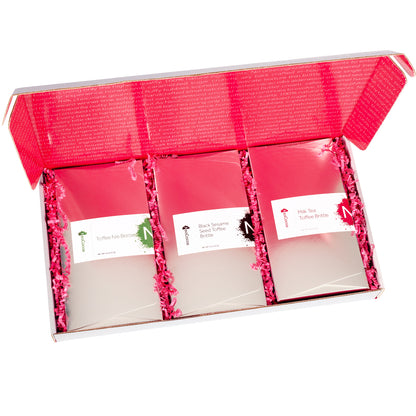 Open rectangle gift box lid up with view of  3 - 8oz silver boxes of brittle with pink crinkle paper cushion between the boxes. 