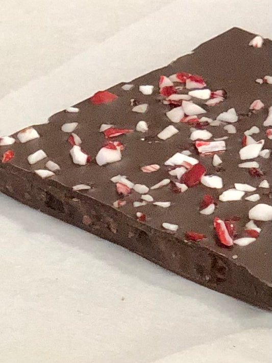 Close up of one piece of peppermint toffee nib brittle with ground pieces of peppermint candies on top of chocolate