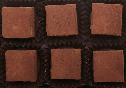 View from above of the opened “Zested Lime” with six cube-shaped chocolate truffles arranged in two rows, 3 truffles per row, each in paper candy cup. 