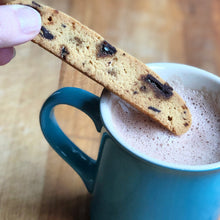 Load image into Gallery viewer, 1 sesame brittle biscotti being dunked in a mug of hot chocolate.